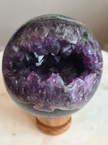 Amethyst geode sphere 930g, 9.2cm, from Brazil on wooden stand – front view of deep purple crystal cavity