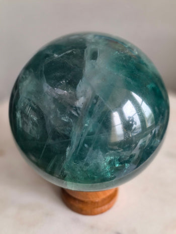 Green fluorite crystal ball with translucent sea-green planes and white veils