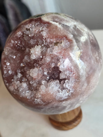 Angled view of pink amethyst crystal ball with large rose-pink geode pocket