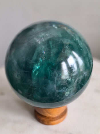 Teal glow inside a polished green fluorite sphere with rainbow flashes