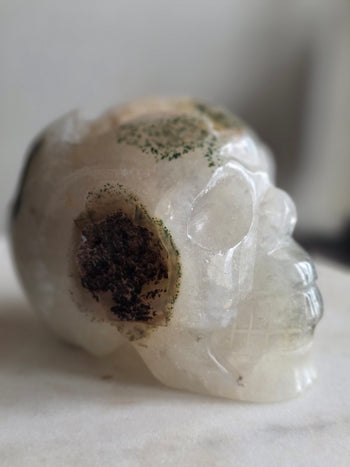 Side of moss agate skull showing a dark sparkling druzy cavity ringed with green moss