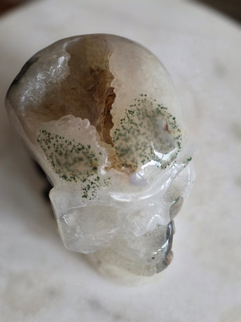Top of moss agate crystal skull with green moss spots and an open geode pocket
